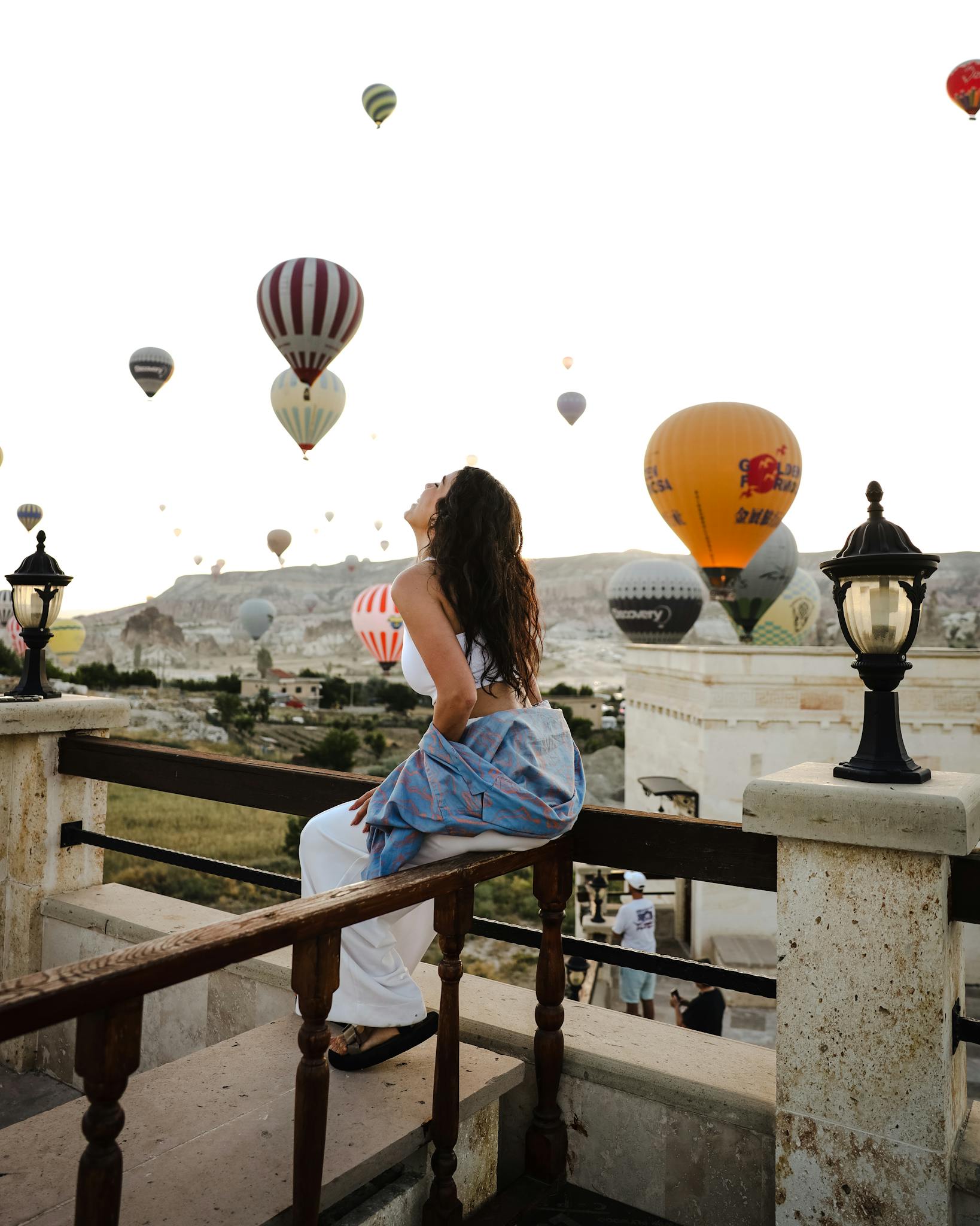 Woman on balcony watching hot air balloons in Cappadocia, Turkey at sunrise.